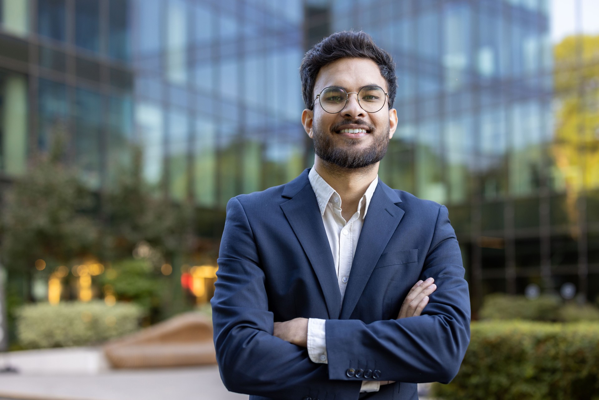 Confident young business professional standing in front of modern office building with arms crossed